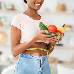 Healthy nutrition for weight loss. Black lady with tape measure holding bowl of fruits and